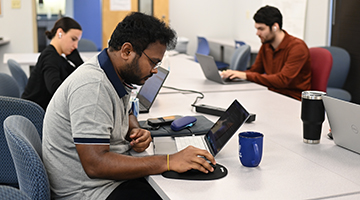 Three graduate computing students working on their laptops in a study room