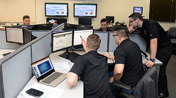 A group of UNF students in a room full of computers that have different data graphs on their screens