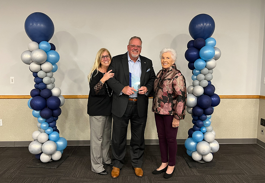 John Wagner holding his award standing between his wife and mom