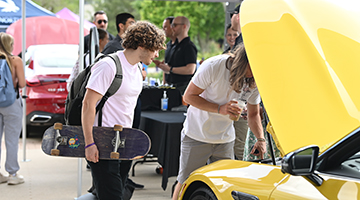 Students looking into the hood of a yellow Mercedes