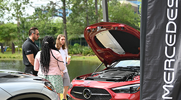 Two students speaking with a Mercedes employee while looking at a red Mercedes
