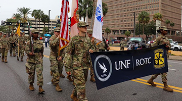UNF ROTC marching downtown holding a UNF ROTC banner