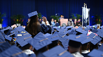 A single student standing up among rows of caps