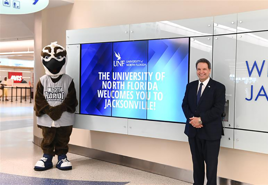 President Moez Limayem and Ozzie at the airport in front of a UNF bulletin screen