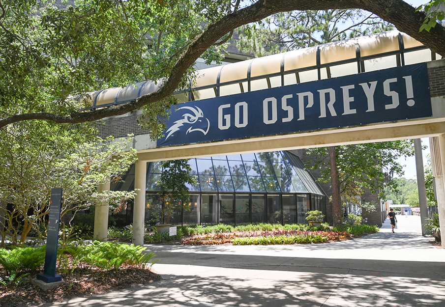 Campus scene outside of Carpenter Library near the Starbucks with a 'Go Ospreys!' sign hanging from balcony