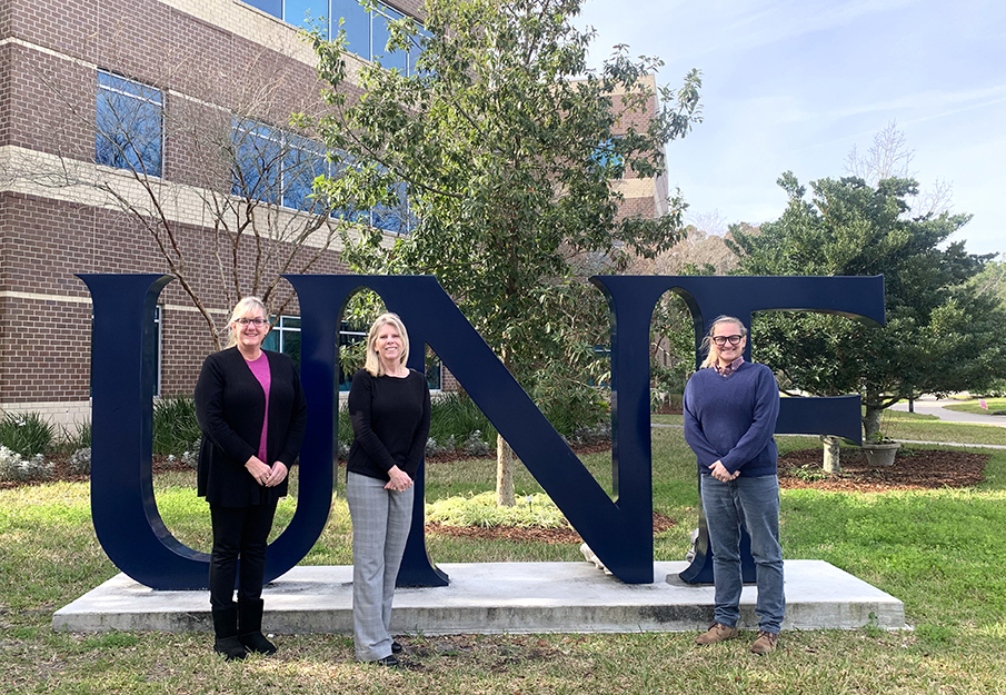 Three UNF faculty standing in front of the UNF letter sign