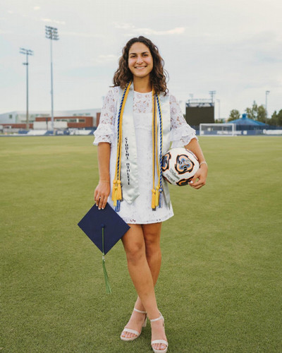 Zara Siassi graduation photo standing on soccer field with hat, tassels and soccer ball