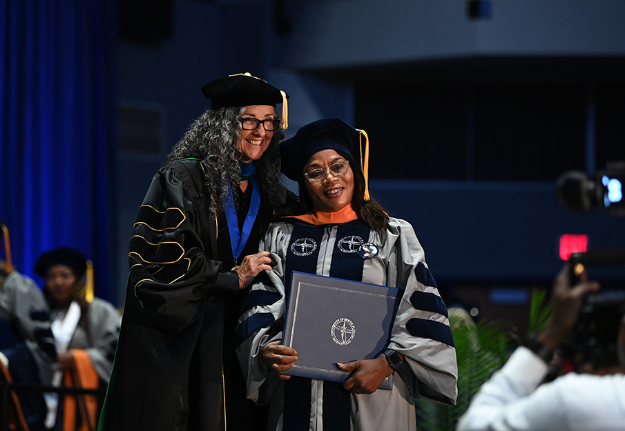 Professor and graduate student posing with a degree at commencement
