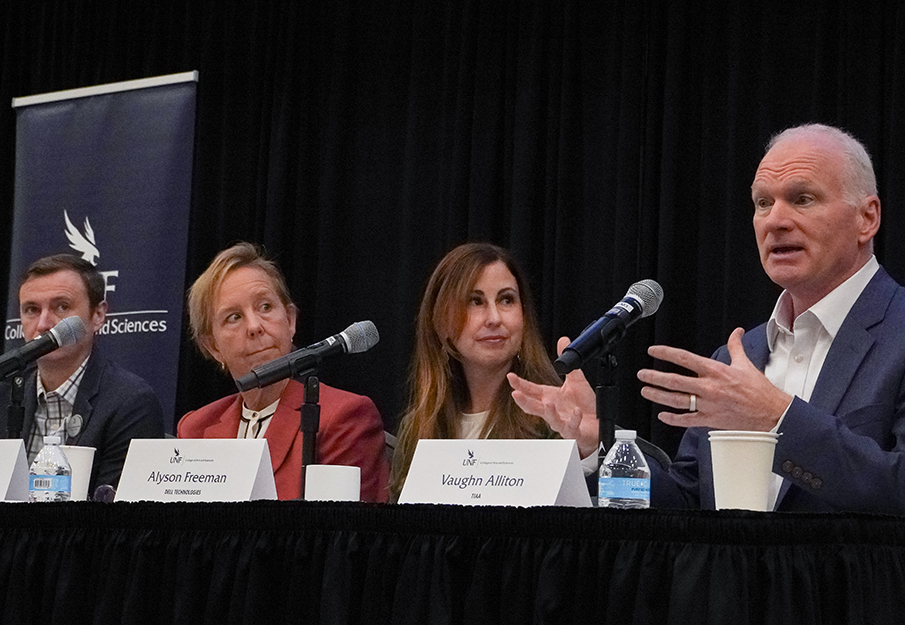 Four guest panelists sitting behind table with mics