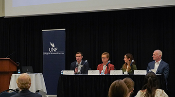 Four guest panelists sitting behind table with mics