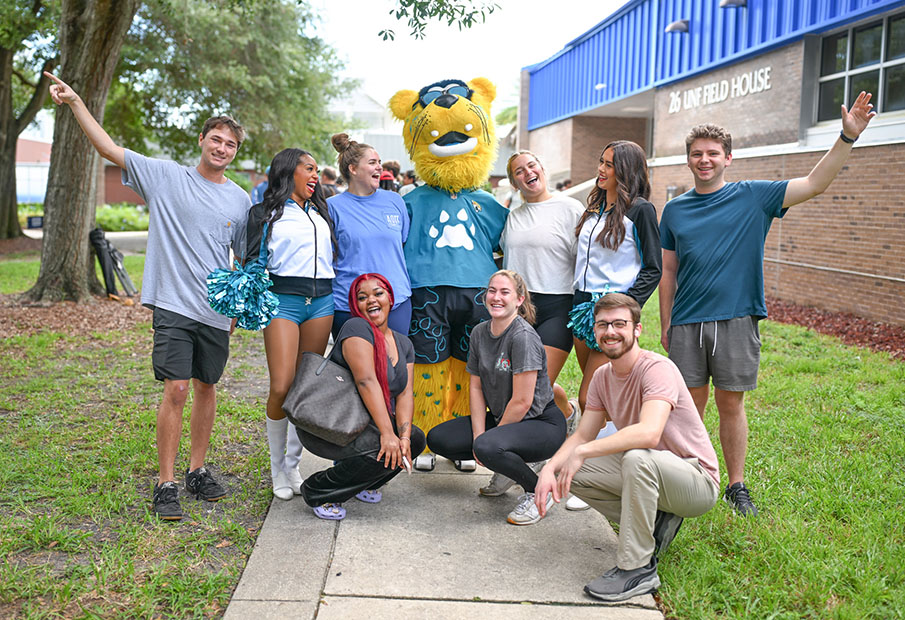 UNF students posing with Jacksonville Jaguars mascot and two cheerleaders outside the UNF Field House