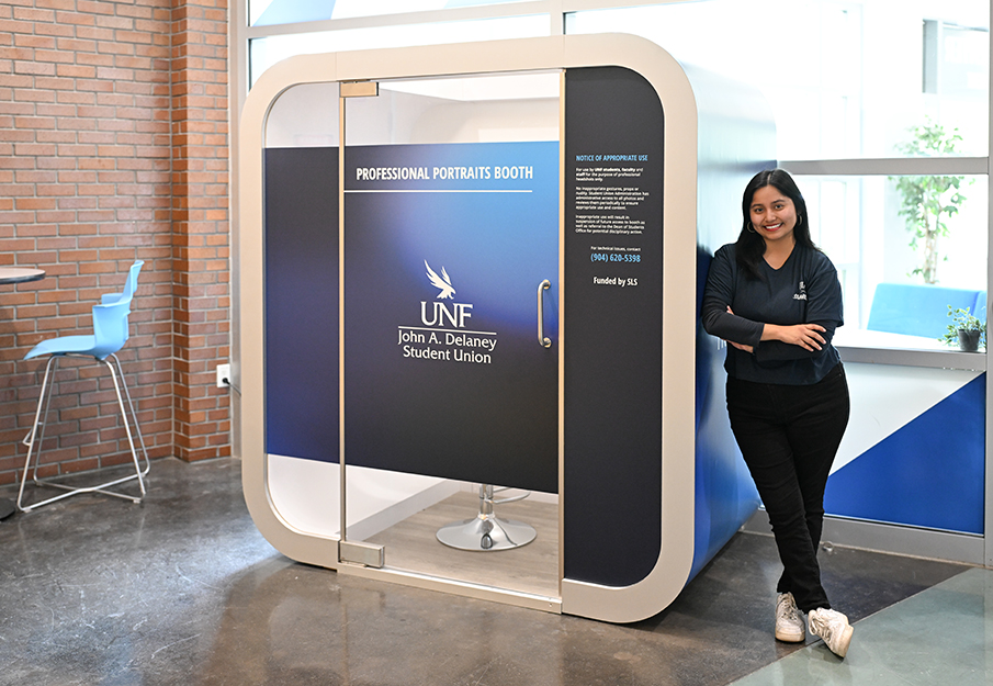 UNF student posing next to the Professional Portraits Booth in the Student Union