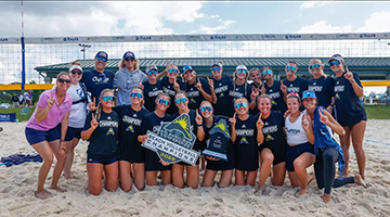 The Beach Volleyball team standing in front of volleyball net holding ASUN sign