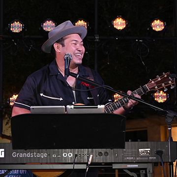 Andrew Sabin sitting behind a keyboard holding a guitar