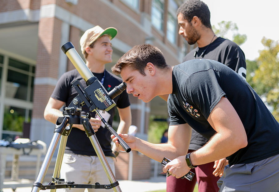 Three students standing around a telescope
