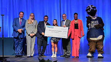 President Moez Limayem, Ozzie, staff and a student on stage holding a First Coast check