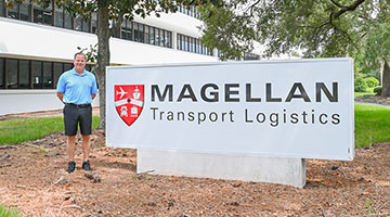 Tom Piatak standing near Magellan Transport Logistics sign in front of building