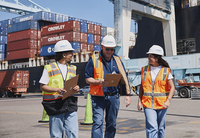 Two UNF transportation and logistics students speaking to a professional at a shipyard