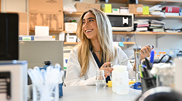 Anne Araujo putting a solution in a bottle in a lab while smiling