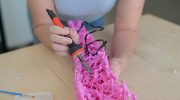 Upclose image of Emily Bailey working on melting toy pink soldiers with tool