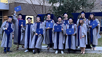 Brenna Brisson posing with her Global MBA cohort in front of UNF letters wearing graduation garbs