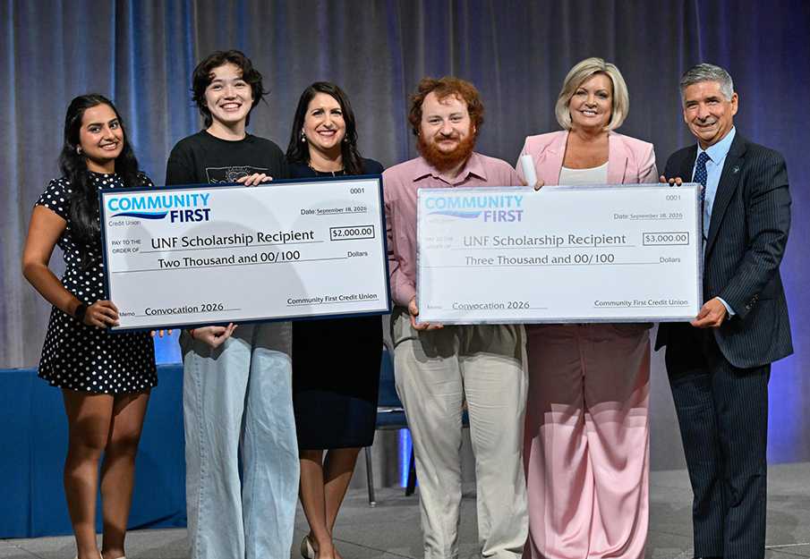 Two student scholarship recipients stand with checks and Community First Credit Union leaders