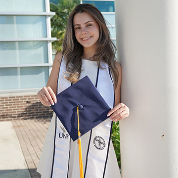 Erina Kotreli holding her graduation cap leaning against a pillar
