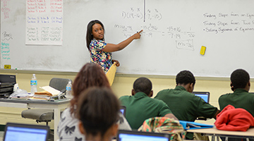 UNF student teaching math at a white board in front of a room of Duval students