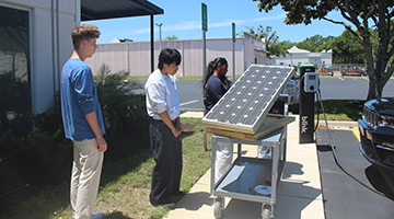 UNF students looking at solar panel next to electric car charging station