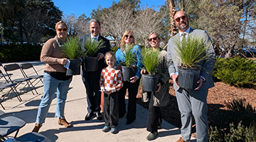 President Moez Limayem standing beside a family holding potted tree saplings