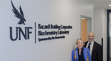 Two donors of the UNF chemistry lab standing next to the lab's entrance sign