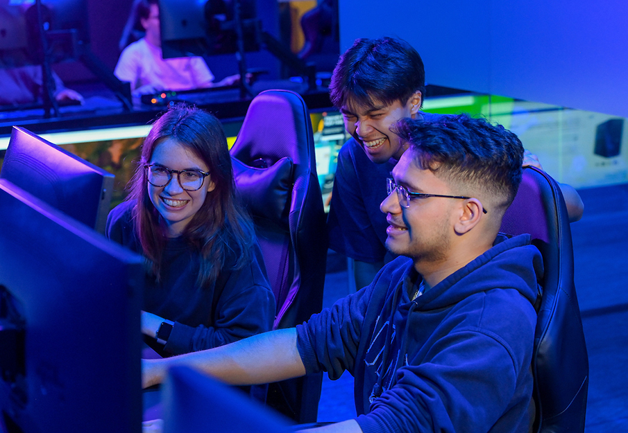 Three UNF students crowding around a computer playing a video game