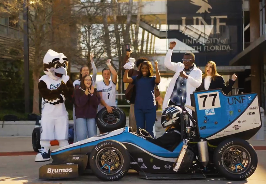Ozzie and UNF students cheering on race car in front of Student Union