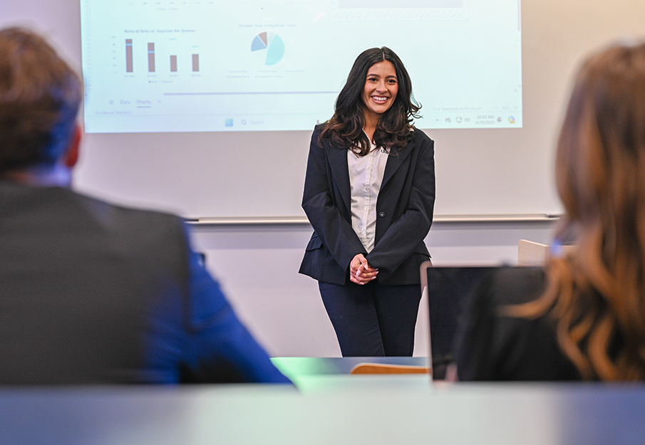 Professor presenting data analytics on a white board while two students sit at desks