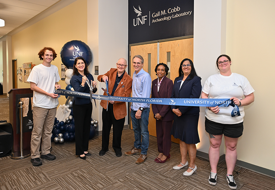 Bill Cobb, UNF archeology professors and students cutting ribbon in front of Gail M. Cobb Archaeology Laboratory entrance