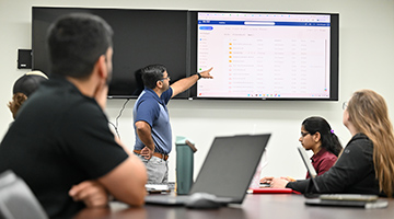 Dr. Vamsi Kalasapudi pointing at a screen in front of a class