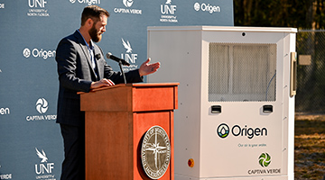 A representative talking at podium next to Origen machine