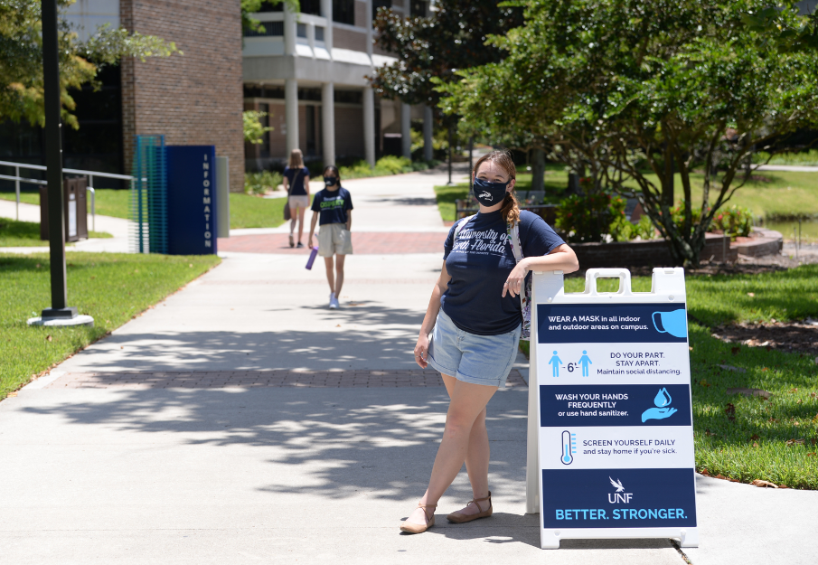 Student wearing a mask in front of the UNF COVID recommendations sign