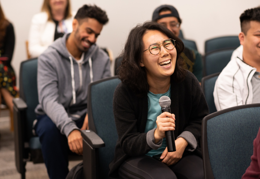 Female holding a microphone talking and smiling in an auditorium