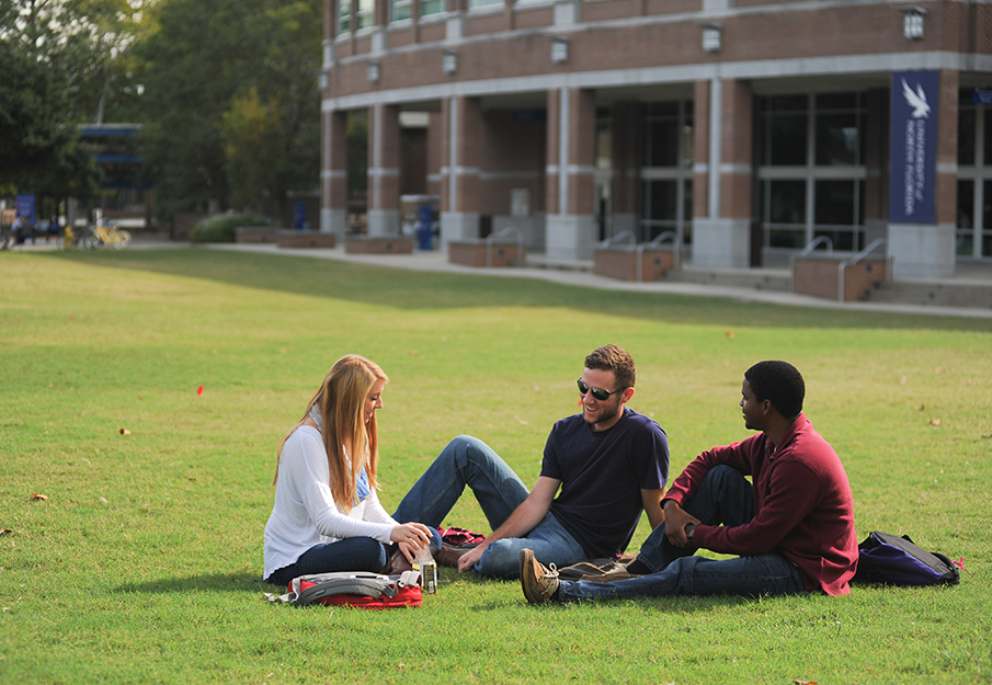 Three students sitting on the green talking