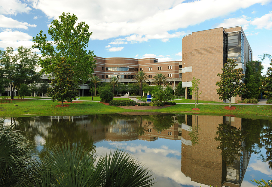 Outside view of the Brooks College of Health building and a small lake