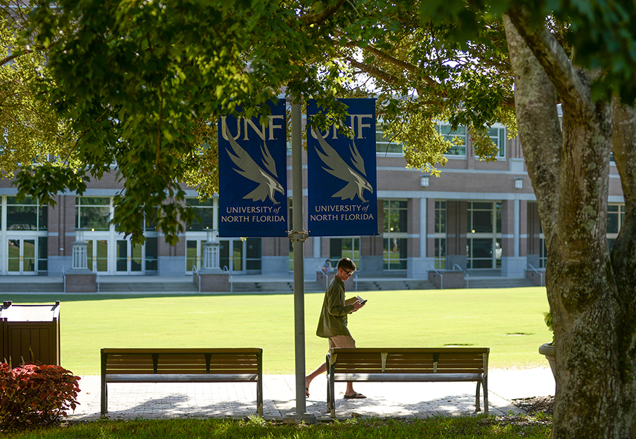 Student walking at the green on campus with UNF banner