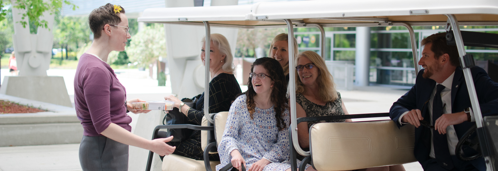 Female OCT student riding on a golf cart with UNF administration and stopped to talk too someone on the sidewalk