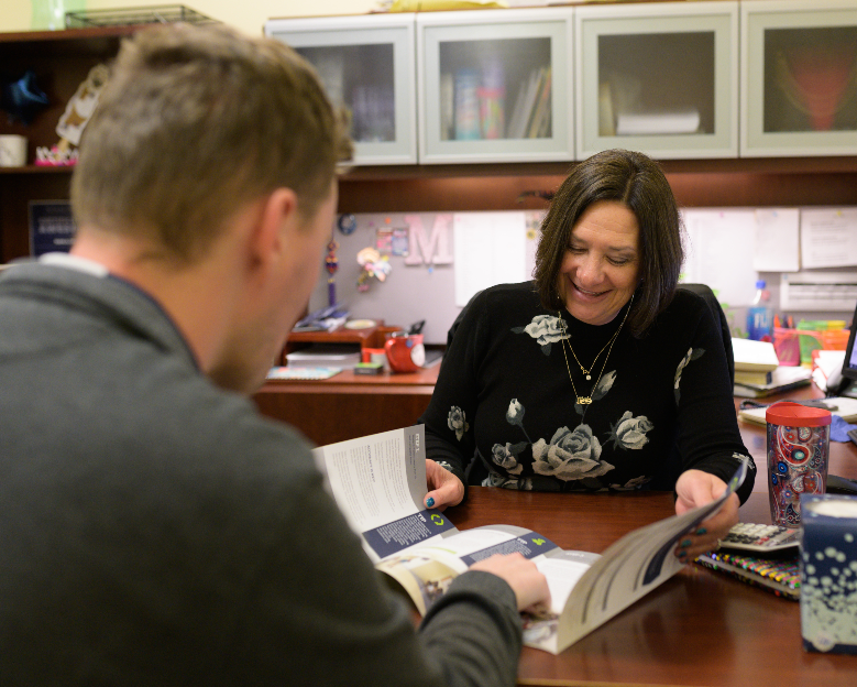 UNF female staff worker in an office looking at an unfolded brochure with a male student