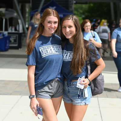 Two female students in UNF t-shirts smiling outside in the student union plaza