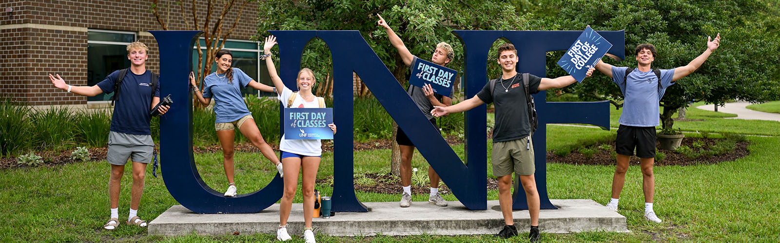 Students holding signs about the first day of classes and first day in college while standing around the UNF sign
