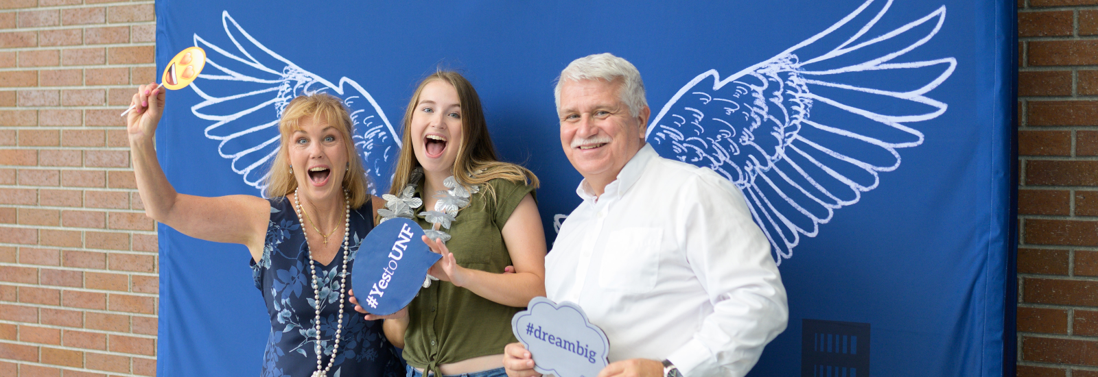 A mother and father with their daughter at a UNF photobooth holding signs up excitedly