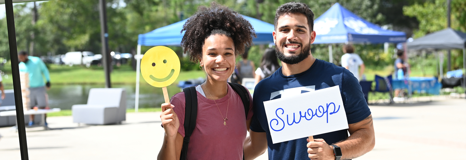 Male and female student holding a smiling face sign and a swoop sign, both smiling