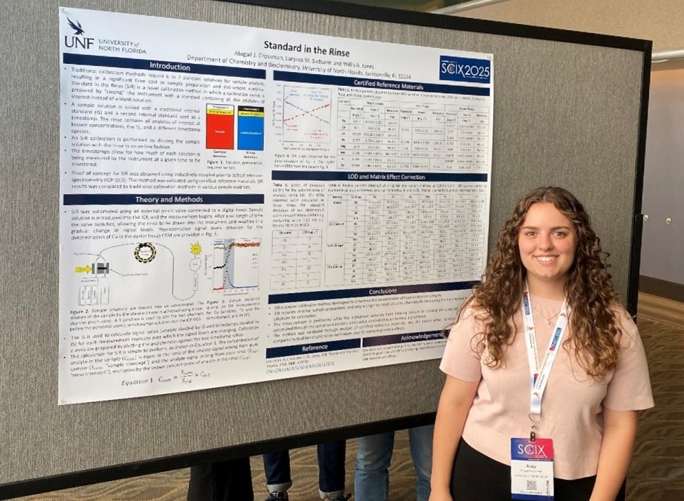 Abby smiling and standing in front of her research poster that is hung up and displayed at a conference venue. 