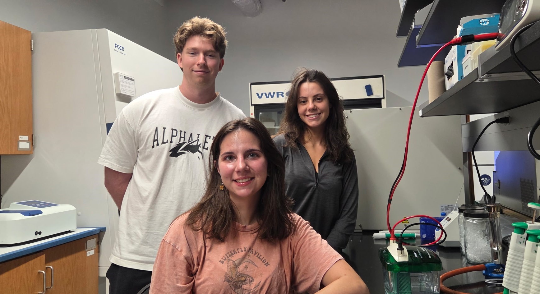 Erina, Lauren, and Zach smiling and posing in their research lab. 